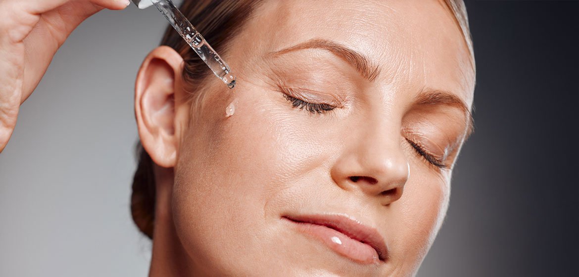 Entspannte Frau trägt sich ein Anti-Aging-Serum mit Hilfe der Pipette in das Gesicht auf